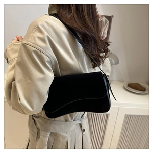 Back view of model wearing black matte shoulder bag with unique wavy flap and beige trench coat
