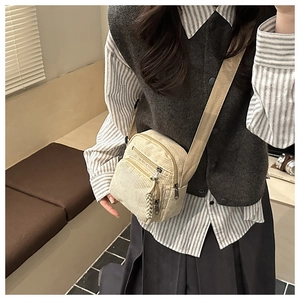 Close-up of cream corduroy crossbody bag featuring a front pocket and woven zipper pull