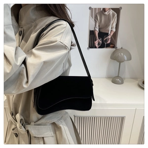 Detail of black velvet shoulder bag with curved bottom on a model in a trench coat