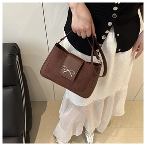 Detail of dark brown shoulder bag with bow buckle and textured mixed leather surfaces