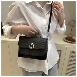 Gros plan du sac besace noir en cuir tressé avec boucle argentée porté par un mannequin