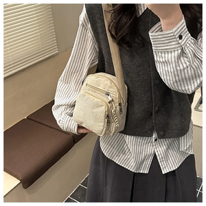 Detail of beige corduroy crossbody bag with multiple zippers and wide strap in casual use