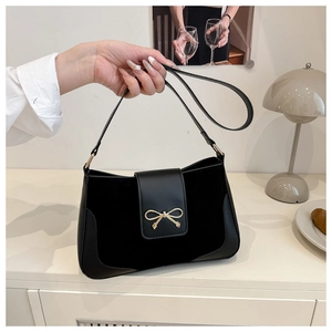 Close-up of black PU leather shoulder bag with a gold bow buckle in a warm lifestyle setting