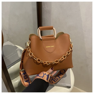 Detail of caramel leather bucket bag with gold chain and wide patterned shoulder strap