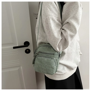 Detail view of light green corduroy fabric texture and zipper pocket on a crossbody bag