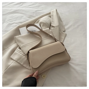 Detail of minimalist beige leather shoulder bag with asymmetrical curved flap and strap