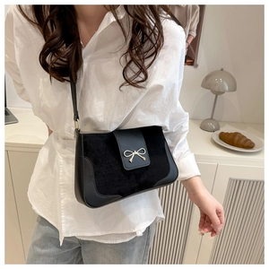 Detail of black crossbody bag featuring suede texture and golden bow magnetic closure