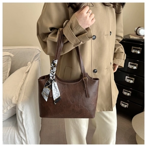 Detail of dark brown leather tote bag with contrast stitching and patterned silk scarf