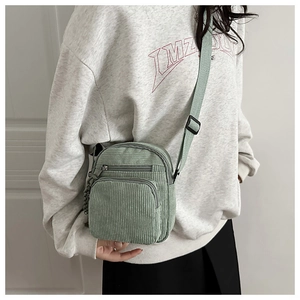 Detail view of light green corduroy crossbody bag with adjustable strap and zip pockets
