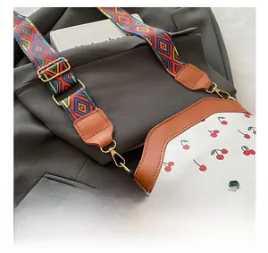 Dettaglio della borsa in pelle bianca con stampa ciliegia e ampia tracolla geometrica