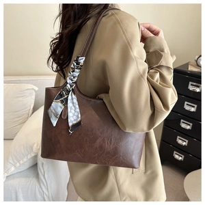 Detail of a dark brown tote bag with decorative silk scarf and textured leather finish