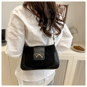 Detail of minimalist black leather crossbody bag with elegant golden bow metal clasp