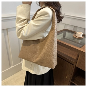 Gros plan d'un sac cabas en cuir tressé kaki clair à l'épaule dans un décor minimaliste