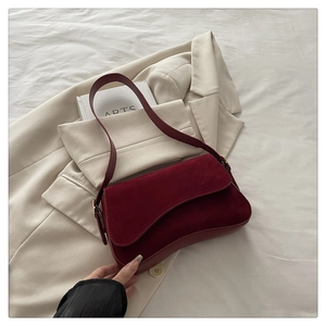 Detail of burgundy suede shoulder bag with flap closure on a beige blazer background