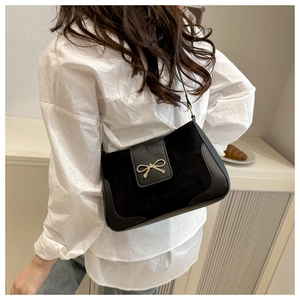 Detail of minimalist black crossbody bag with gold bow clasp on matte texture