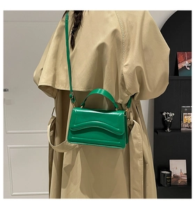 Detailed shot of green leather crossbody bag with wave stitching and gold hardware on model