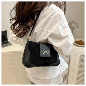 Detail showing smooth leather and suede texture of black shoulder bag with gold bow clasp