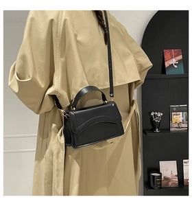 Detail of minimalist black leather square bag with wave-edge flap and gold metal buckles