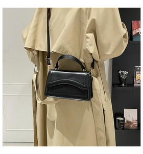 Detail view of black faux leather crossbody bag with gold hardware on a beige coat