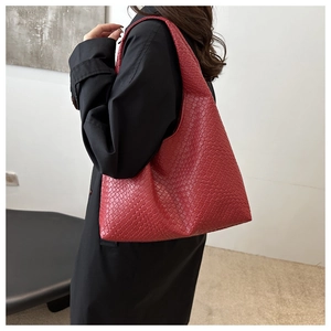 Détail du sac hobo rouge tressé à damier porté par un mannequin en manteau noir