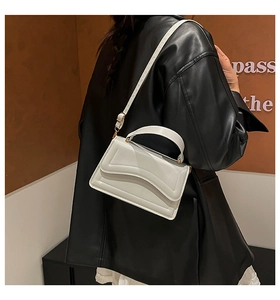 Detailed view of white minimalist handbag with wavy layered stitching and gold hardware