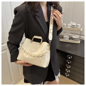 Detail of cream bucket bag featuring decorative chain, metal handle and jacquard strap