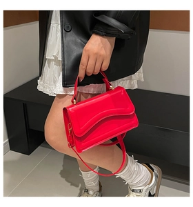 Detail of red patent leather handbag featuring unique wavy edge and adjustable shoulder strap