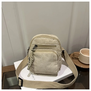 Minimalist beige corduroy crossbody bag with multiple zippers and wide strap in casual setting