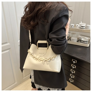 Detail of white leather bucket bag with gold handle and decorative chain on a model