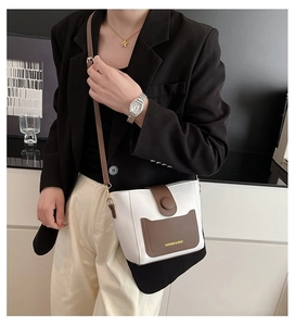 Detail of a contrast color bucket bag with white body, brown flap, and adjustable strap
