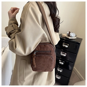 Minimalist dark brown corduroy crossbody bag with multiple zippers shown on a beige coat