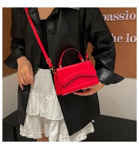 Detailed view of red leather crossbody bag with gold buckle on model in black jacket