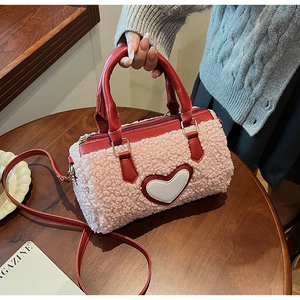Close-up of pink lamb wool cylinder bag featuring a white heart patch and red leather handles