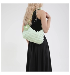Detail of light green popcorn textured cylinder bag with daisy charm on a model