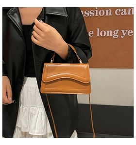 Detail of a brown leather shoulder bag with a unique wavy stitch on the flap cover