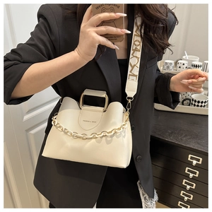 Detail of cream white bucket bag with wavy edge, gold handle, and resin chain strap