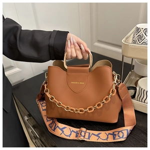 Detail of caramel bucket bag featuring metal handle and blue geometric printed strap