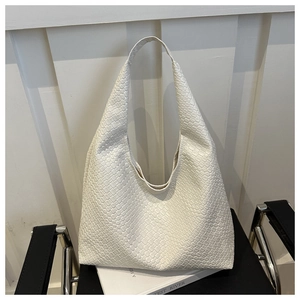 Gros plan du sac hobo blanc à texture tressée posé sur un siège en cuir noir élégant
