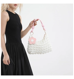 Detail of white popcorn textured bucket bag with pink braided handle and floral charm