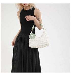 Detail of white quilted bucket bag with green woven handle and floral charm accessory