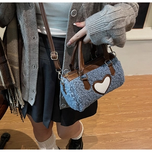 Detail of blue faux shearling barrel bag with white heart patch shown on a model