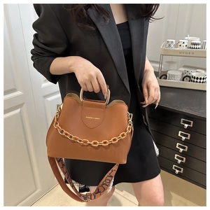 Detail of brown leather bucket bag with gold chain handle and wide patterned shoulder strap