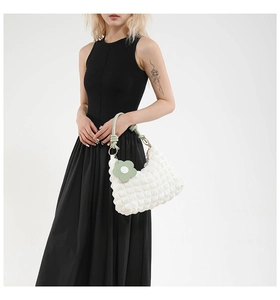 Close-up of white quilted bubble tote bag with green braided handle and flower charm