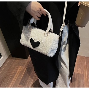 Close-up of white fleece crossbody bag featuring a black heart patch and gold metal clasps