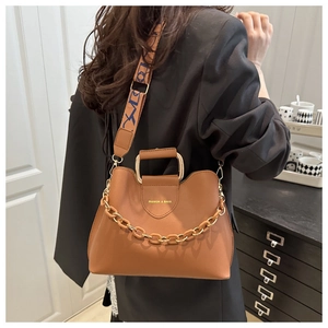 Close-up of caramel brown bucket bag with U-shaped metal handle and golden chain detail