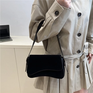 Chic black suede shoulder bag with unique wave flap design in minimalist office setting