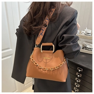 Brown bucket bag detail showing wide patterned strap and gold fashion lettering