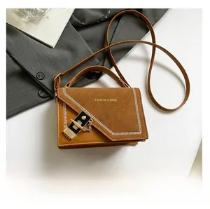 Detail of a brown shoulder bag featuring suede texture and decorative gold chain buckle