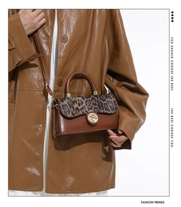 Detailed close-up of leopard print flap bag with gold buckle lock and brown leather handle