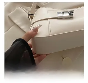 Detail showing precise white stitching and silver square metal lock on cream leather bag
